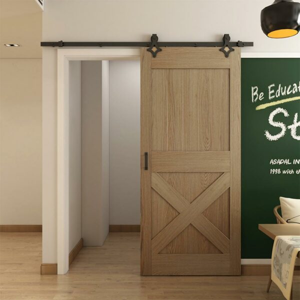 Een houten schuifdeur met zwart staldeurbeslag, ruitvormige vorm, hangende stijl, gedeeltelijk open, waardoor een ingang naar een andere kamer in een modern huis zichtbaar wordt met een schoolbord aan de muur.