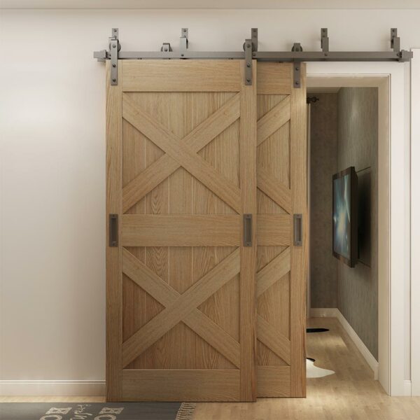 Dos puertas de granero de madera en un sistema de herrajes para puertas de granero de doble derivación se cerraron sobre una puerta en una casa moderna con un pasillo visible detrás.