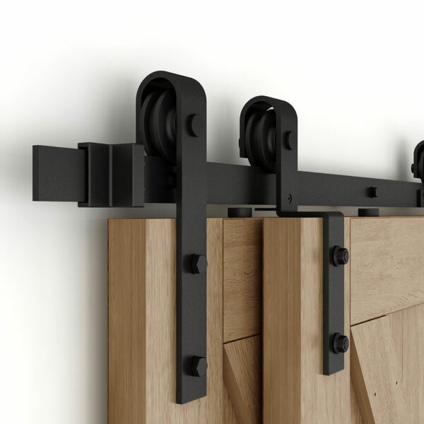 Close-up view of a modern black Top Mount Barn Door Hardware, with Big Wheel, mounted on a wooden door against a white wall.