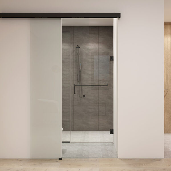 Un bagno moderno visibile attraverso una porta scorrevole in vetro smerigliato parzialmente aperta con un sistema di binari per porte scorrevoli in vetro in alluminio, che mostra una cabina doccia in vetro trasparente con finiture in metallo.