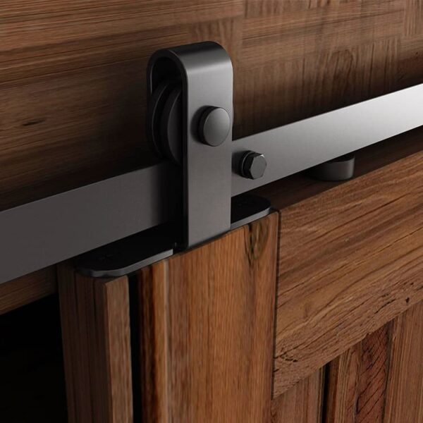 A modern Mini Barn Door Hardware, Top Mount mechanism with a matte black handle and rail, mounted on a textured wooden door and frame.