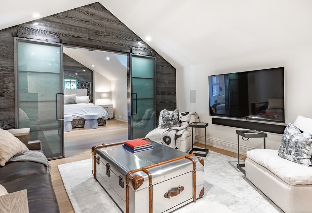 Modern bedroom with sliding barn doors, a seating area, and a wall-mounted television.