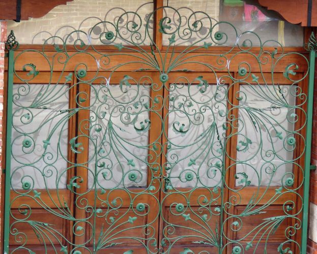 Ornate wrought iron gates with swirling patterns against a brick wall.