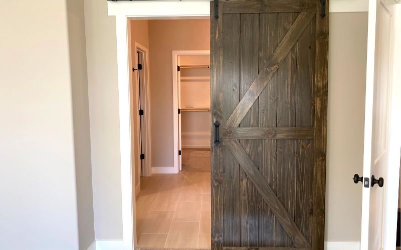 Una puerta rústica de madera de granero parcialmente abierta, que conduce a una habitación con estantes vacíos.