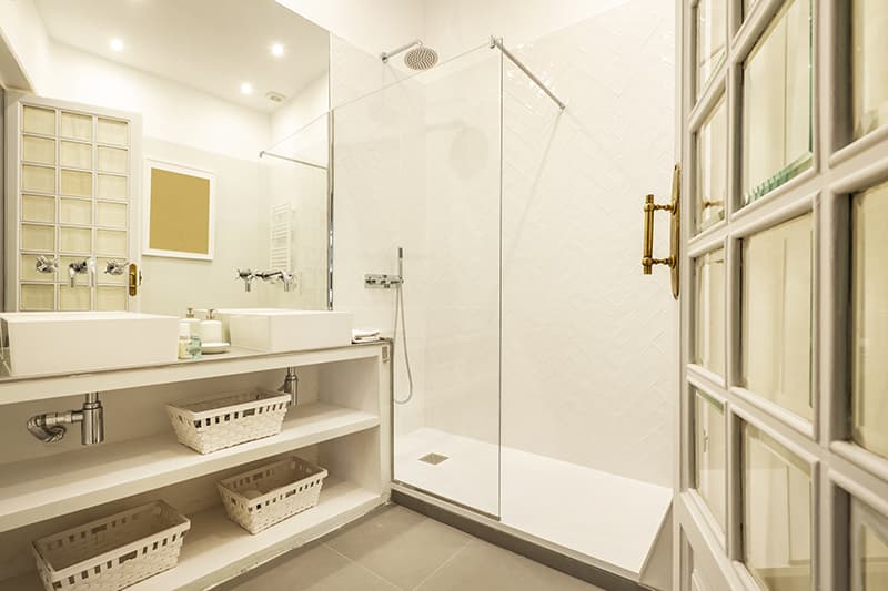 Modern badkamerinterieur met een glazen douchecabine, witte wastafel met twee wastafels en witte rieten manden onder de wastafel, neutrale tinten.