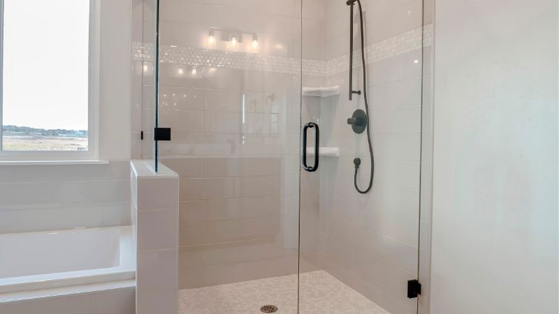 Modernt badrum med en inglasad duschkabin bredvid ett vitt badkar, med svart inredning och neutral kakeldesign.