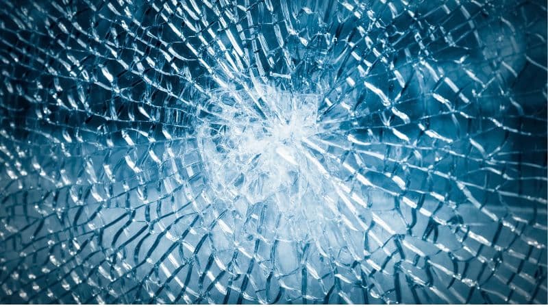 Close-up of a shattered glass window with a sharp focus on the impact point, highlighted by a cool blue tone.