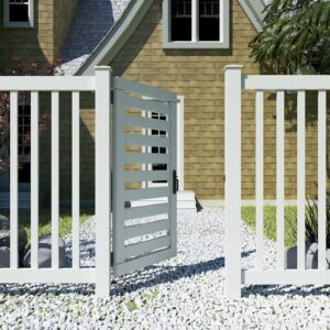 A white wooden fence with an open, latched gate stands in front of a stone house and gravel pathway.