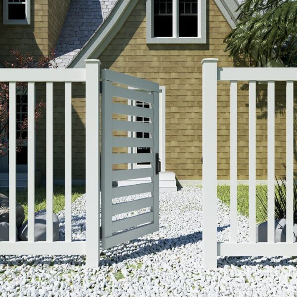 A white wooden fence with an open, latched gate stands in front of a stone house and gravel pathway.