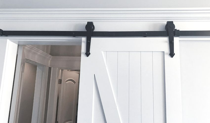 A partially open white barn door on a black track reveals a hallway with several doors.