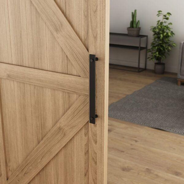 A close-up of the American Vintage Black Barn Door Pull Handle on a wooden sliding door, with plants, a shelf, and rug decor.