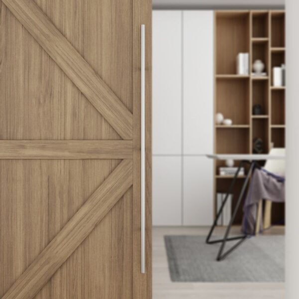 A wooden sliding barn door with a 60-inch stainless steel handle stands out against a modern interior of white cabinets and shelves.