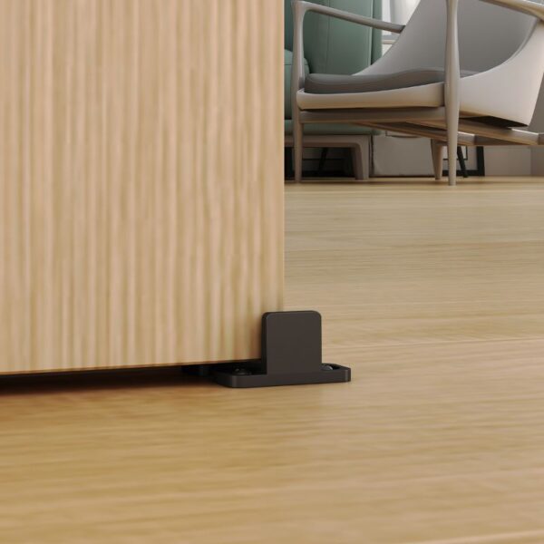 A wooden wall meets a heavy-duty floor, anchored by a doorstop and an adjustable floor guide. A chair is visible in the background.