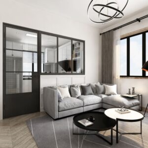 A modern living room with a gray sectional, round tables, and black light. A 3-Lite glass door adds elegance and separates it from the kitchen.