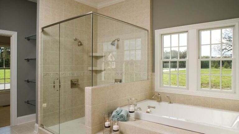 Une salle de bain moderne avec des portes de douche Top 2024, une douche en verre élégante, une baignoire luxueuse, des serviettes moelleuses, des bougies et une vue sereine sur la fenêtre.