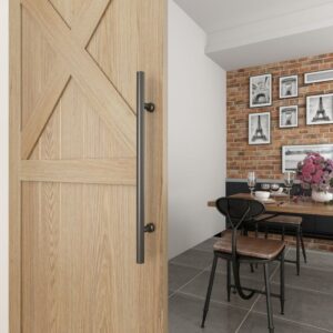 A wooden sliding barn door with a black steel handle opens to a dining area with a brick wall, Eiffel Tower prints, and a table.