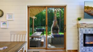 View through top 10 sliding door shows covered patio with picnic table, grill, fireplace among trees; dining area inside.