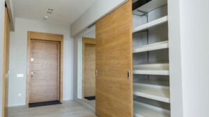 Entrada moderna con puertas de armario de madera de primer fabricante, espejo grande, paredes claras y estantes blancos vacíos.