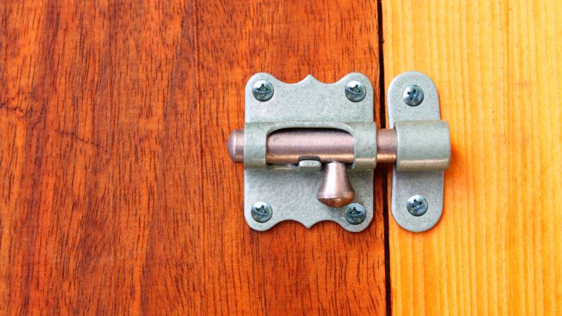 Gros plan d'un loquet de porte en métal sur deux panneaux en bois, l'un foncé et l'autre clair, tirés de notre guide des loquets de porte.