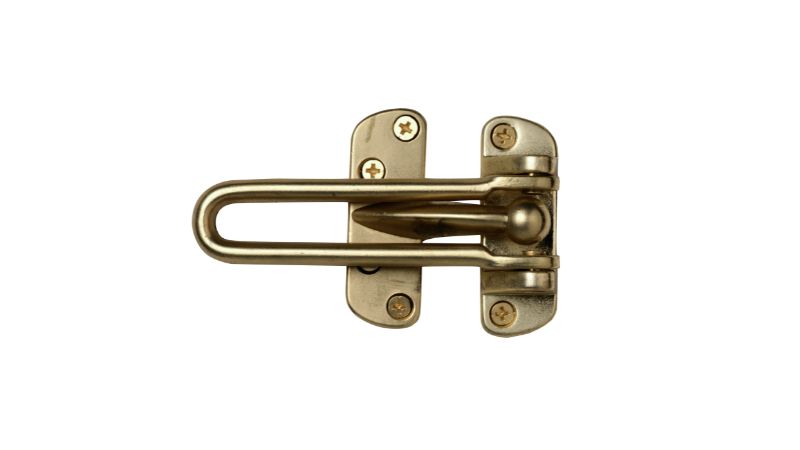 Un loquet de porte à barre pivotante en laiton est monté sur un fond blanc.