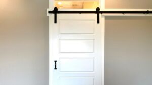 White sliding barn door with black hardware and transom window above, ideal for modern, seamless installation.