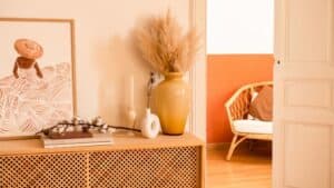 A sideboard with vases, art, and branches stands by an open door showing a rattan chair—showcasing rich textures.