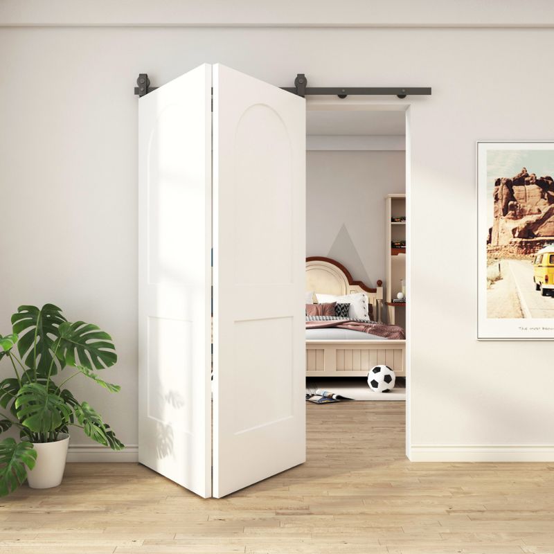 Une porte de grange pliante blanche s'ouvre sur une chambre confortable avec un lit, un ballon de football, du parquet, une plante et des œuvres d'art murales encadrées.