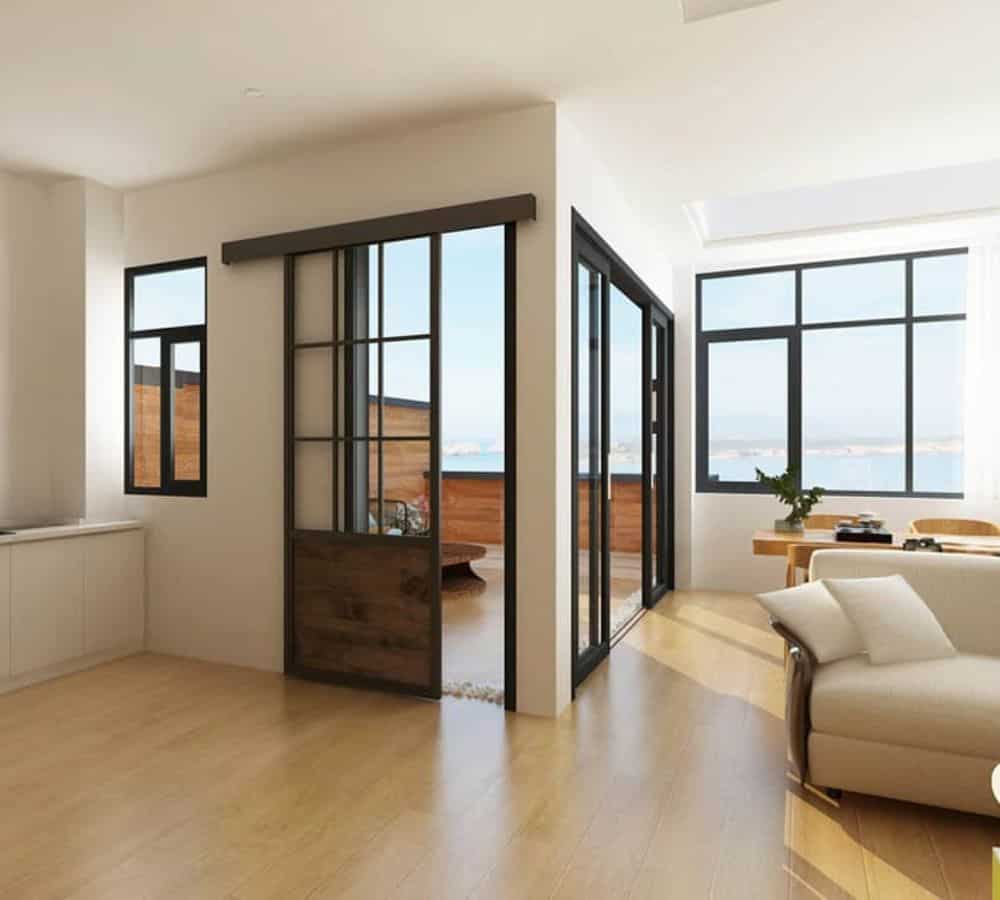 Moderna sala de estar con pisos de madera, ventanas grandes, puertas de vidrio al patio y al agua, muebles neutros y luz natural.