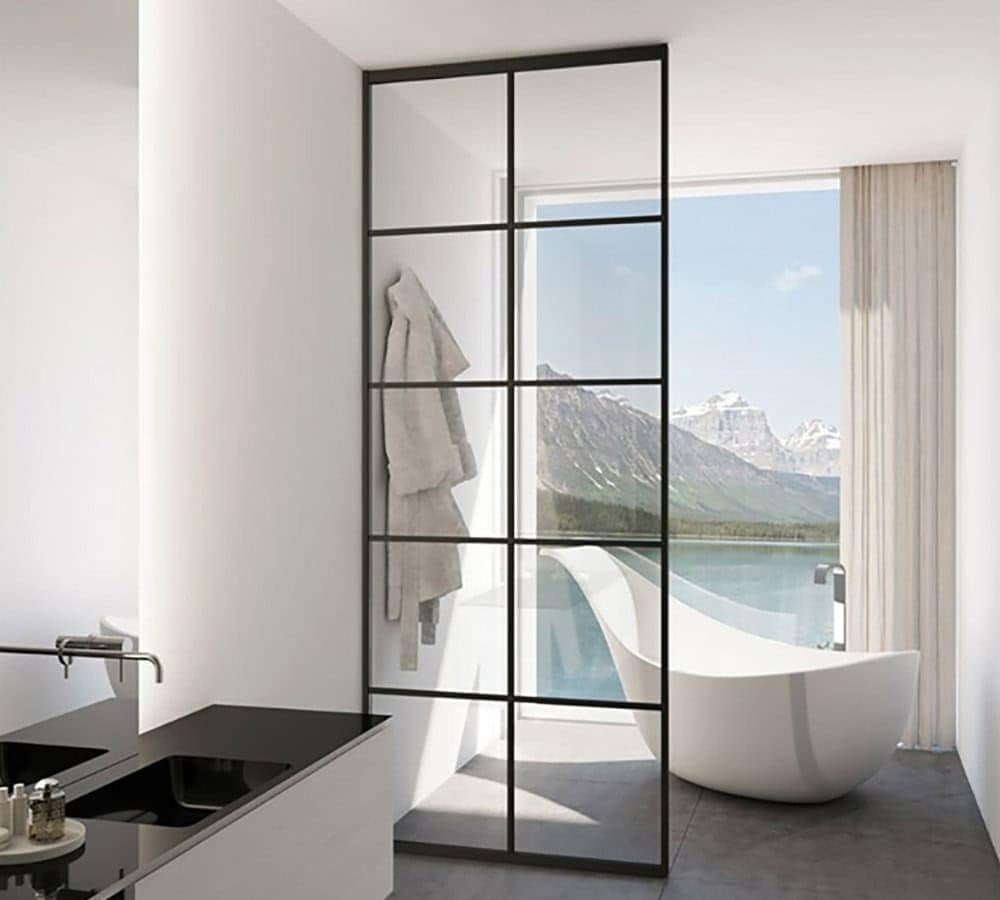 Baño moderno con bañera independiente, mamparas de cristal, albornoces colgantes y un gran ventanal con vistas a las montañas y al lago.