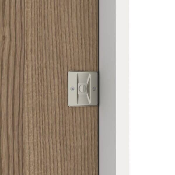 Gros plan d'une serrure de porte coulissante en nickel brossé sur une porte en bois à côté d'un cadre blanc.