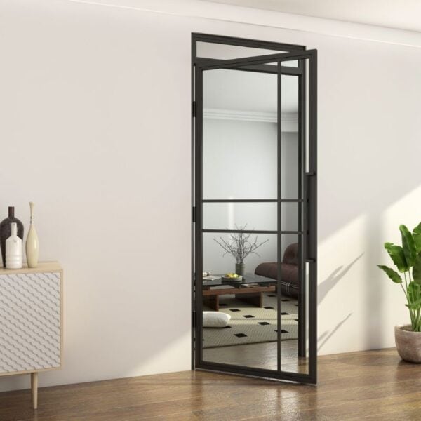 Open steel and glass door with fanlight links hallway with cabinet and plant to a living room with sofa, table, and rug.