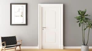 White mould-pressed door centered in a gray wall, with a picture, black chair, and tall plant on a wooden floor.