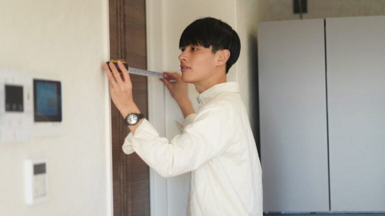 Pessoa medindo a moldura da porta para instalação de porta de celeiro usando uma fita métrica, garantindo dimensões precisas para encaixe e funcionamento adequados.