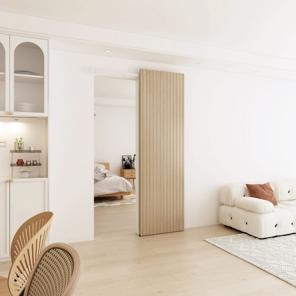 Bright and airy minimalist living room with white walls, a white sofa with brown cushions, and a wooden sliding door leading to a bedroom.