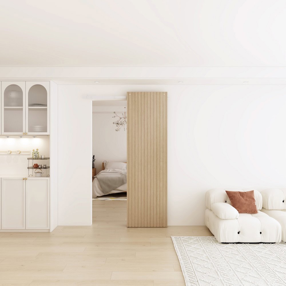Bright and airy living room with white walls, a white sofa with brown cushions, and a wooden sliding door leading to a bedroom.