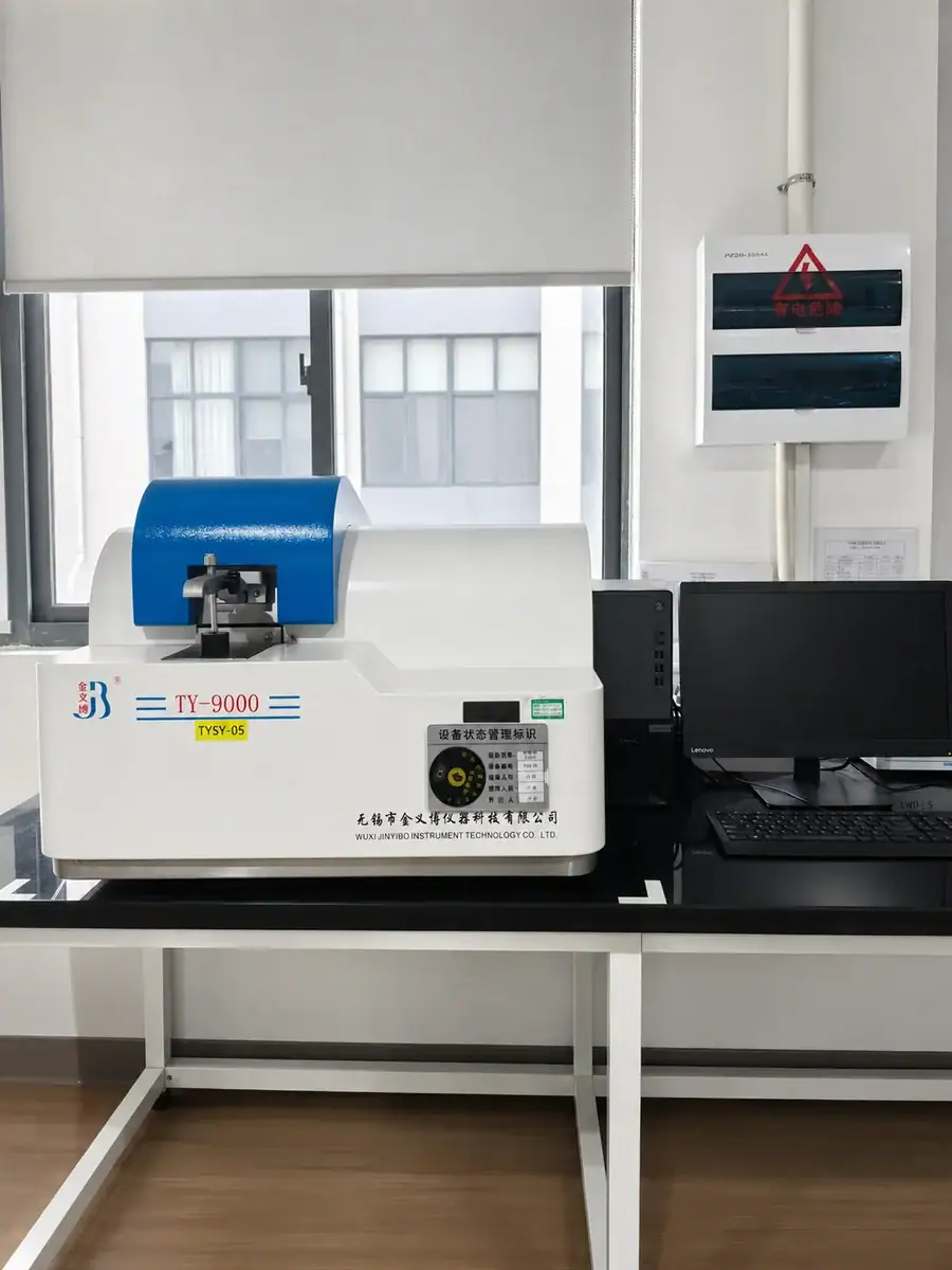 Laboratory machine with blue and white design placed on a table near a window, with a computer monitor and safety box on the side.