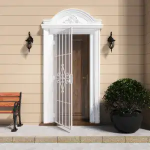 Elegant white security screen door with scrollwork design and expanded metal mesh, installed on a beige exterior wall with decorative trim and outdoor lighting.