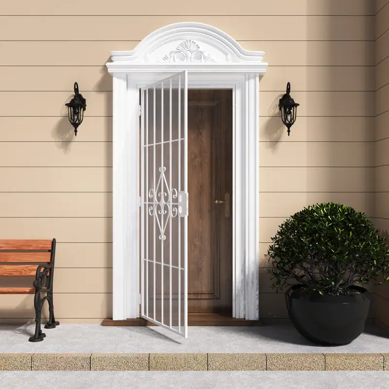 Elegant white security screen door with scrollwork design and expanded metal mesh, installed on a beige exterior wall with decorative trim and outdoor lighting.