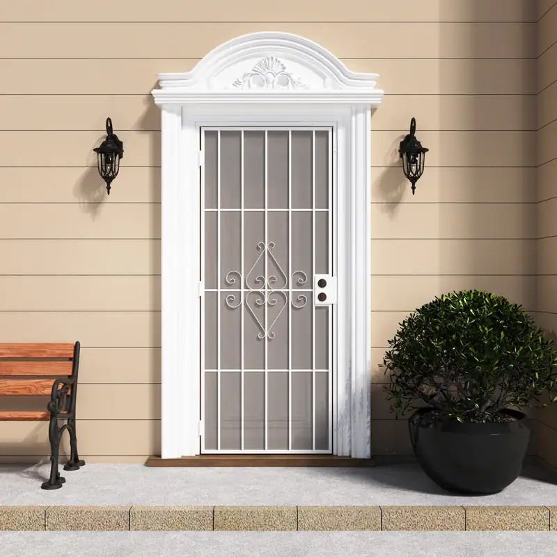 White security screen door with decorative scrollwork and expanded metal mesh, installed on a beige house exterior with black wall-mounted lanterns and a potted shrub.